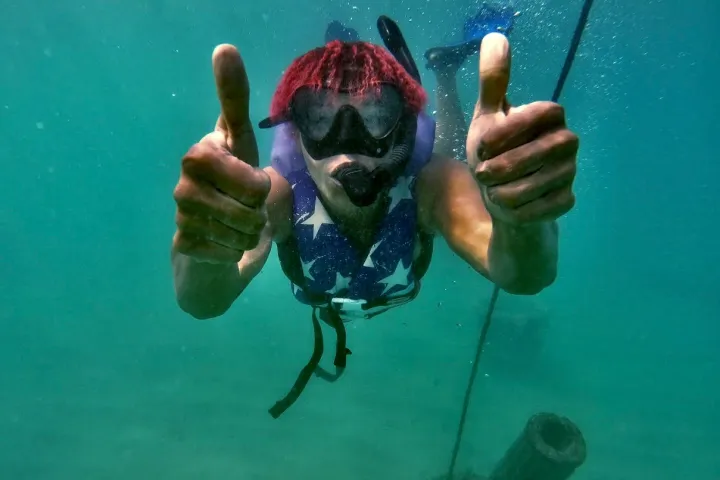 Person underwater with snorkel mask giving thumbs up to camera.