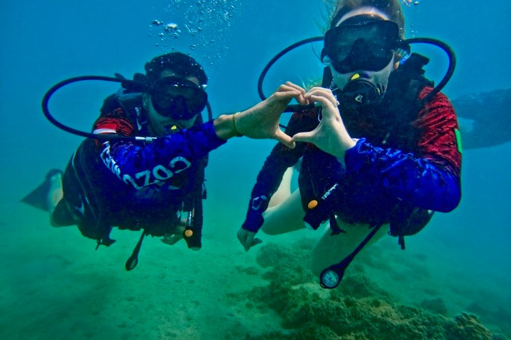 Two scuba divers underwater making heart shape with hands.