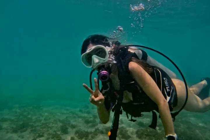 Scuba diver underwater giving a peace sign, surrounded by blue water.