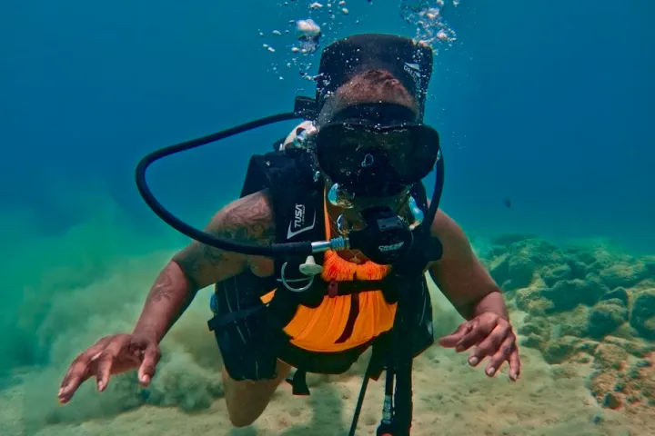 Scuba diver underwater with black gear, bubbles rising.