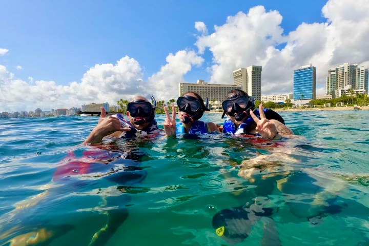 Three people snorkeling and posing in ocean near urban beach with buildings.
