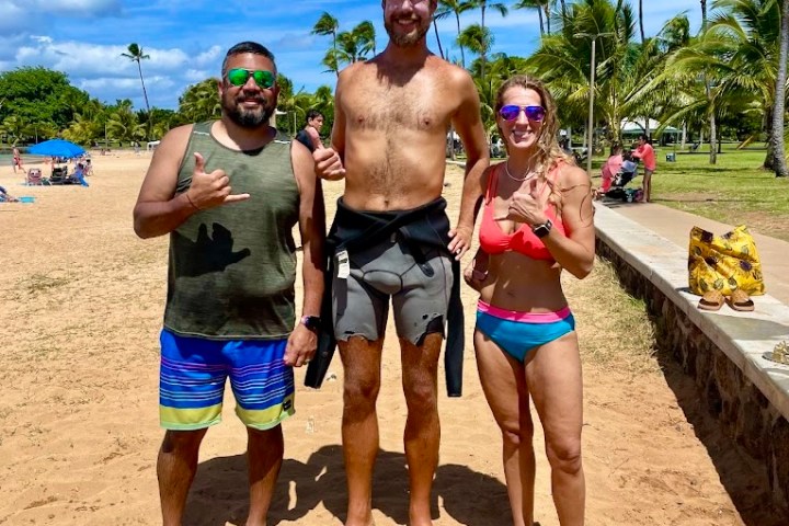 Three people posing on a sunny beach with palm trees in the background.