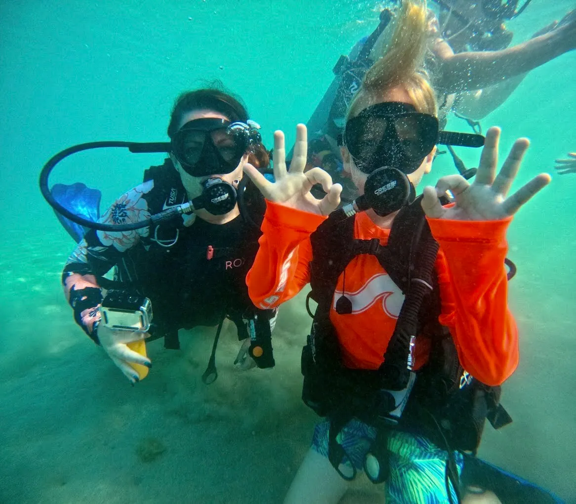 Two scuba divers underwater giving an OK hand sign.